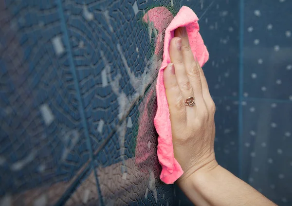 Женская рука, стирающая голубую плитку на стене — стоковое фото