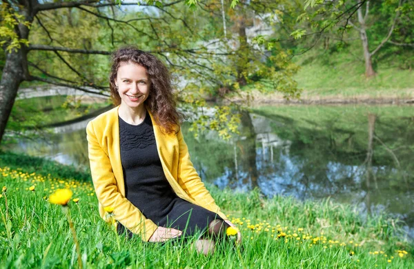Mladá žena, sedící v trávě vedle rybníka — Stock fotografie