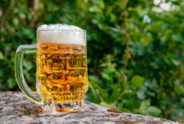 Caneca de vidro com cerveja em pé sobre a pedra grande — Fotografia de Stock