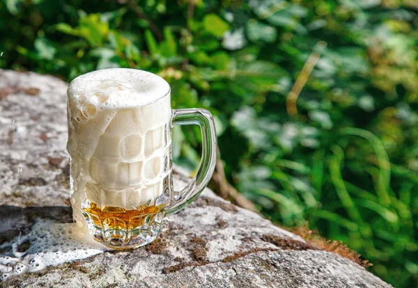 Caneca de vidro com cerveja em pé sobre a pedra grande — Fotografia de Stock