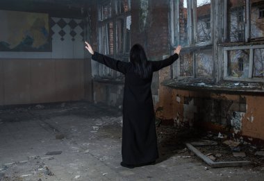 Gotik esmer kadın ellerini kaldırıyor. Karanlık, terk edilmiş evin penceresinin yanındaki boş salonda dikiliyor.