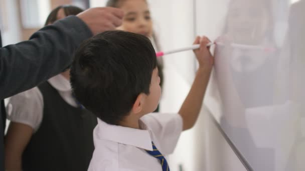 Schoolgaande kinderen schrijven aan boord met leraar — Stockvideo