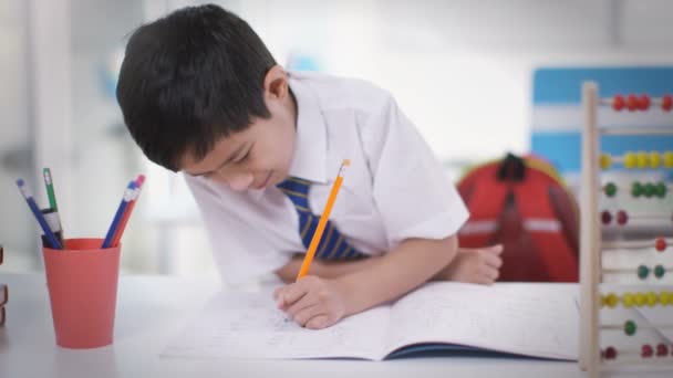 Junge im Klassenzimmer schreibt in Schulheft — Stockvideo