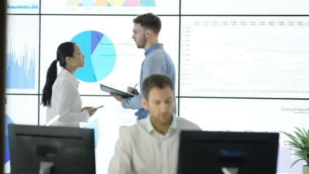 Équipe d'affaires 4K en discussion, regardant les données financières sur l'ordinateur et le mur vidéo 