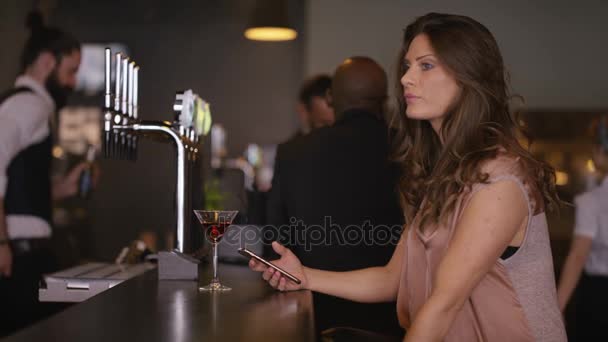 女人在酒吧里等一个迟到的朋友 她检查她的电话 看手表 — 图库视频影像