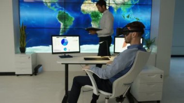 4k işadamı, fütüristik office sanal gerçeklik kulaklık ile etkileşim gösteren finansal bilgi ve Dünya Haritası bilgisayar ekranları