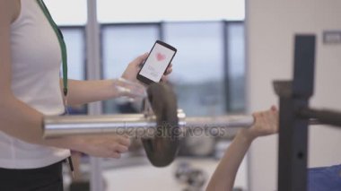 Spor salonunda bir müşteri ile akıllı telefon App-e doğru tren kullanarak fitness eğitmeni