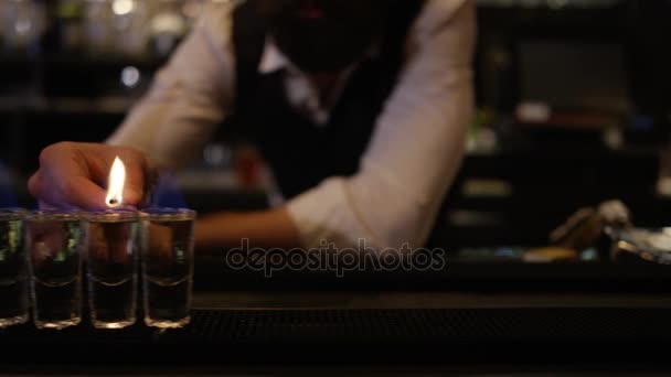 透明な酒でショットグラスの列に光を設定するためにマッチを使用して笑顔のバーマン — ストック動画