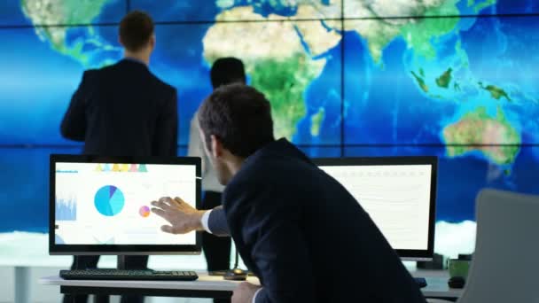 商务团队讨论视频墙上的大型世界地图图形 并在计算机屏幕上显示饼图和图形 — 图库视频影像