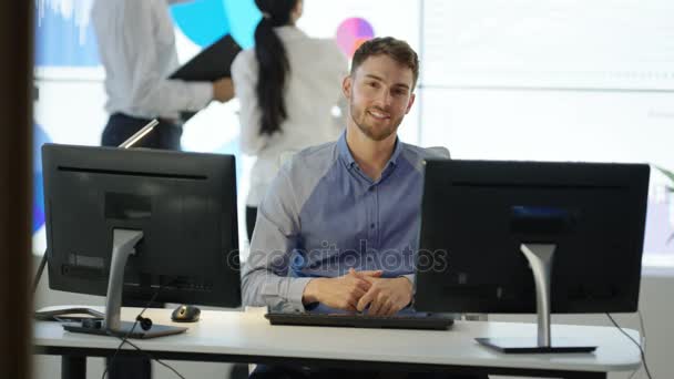 肖像微笑的商人工作在他的办公桌与同事在后台 — 图库视频影像