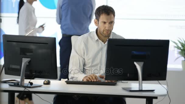 在办公桌前与同事一起在电脑上工作的成熟的商人在后台看视频墙 — 图库视频影像