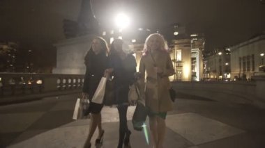4 k mutlu kadın arkadaş alışveriş torbaları şehrin içinden geceleri yürüyen grubu.