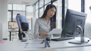 4k telefonda konuşurken ve şirket ofisi içinde bilgisayar üzerinde çalışan bir işkadını
