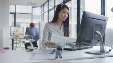 4k telefonda konuşurken ve şirket ofisi içinde bilgisayar üzerinde çalışan bir işkadını