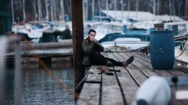 Marina iskele üzerinde tek başına oturmak ve armonika çalmaya 4 k engebeli hipster adam