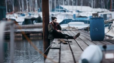 Marina iskele üzerinde tek başına oturmak ve armonika çalmaya 4 k engebeli hipster adam