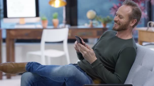 Щасливий Чоловік Розслабляється Вдома Смс Або Використовує Інтернет Своєму Смартфоні — стокове відео