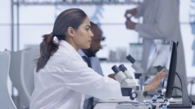 mikroskop altında bir slayt bakarak ve bilgisayarda çalışan 4 k tıp araştırmacısı