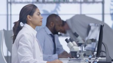 mikroskop altında bir slayt bakarak ve bilgisayarda çalışan 4 k tıp araştırmacısı