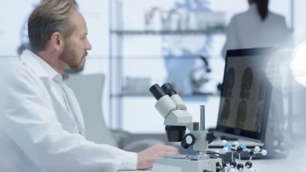 4K Chercheur médical regardant une diapositive au microscope et travaillant sur ordinateur 