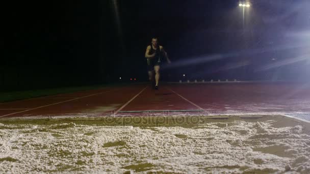 Entrenamiento Salto Largo Masculino Pista Atletismo Oscuridad Bajo Lluvia — Vídeo de stock