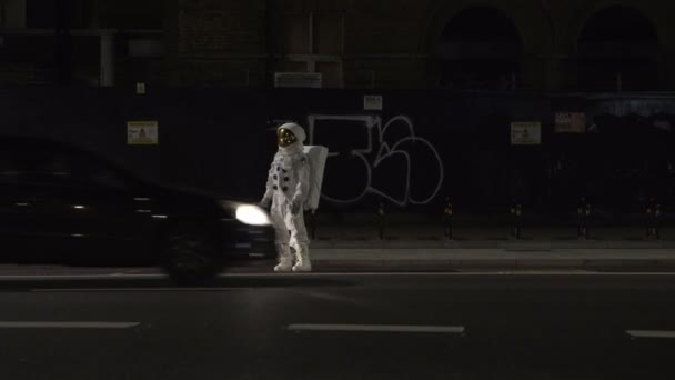 Астронавт Полном Скафандре Пересекает Оживленную Городскую Улицу Ночью — стоковое видео