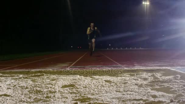 在雨中黑暗的田径跑道上进行男跳远运动员训练 — 图库视频影像