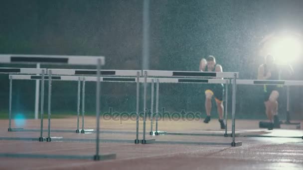 Atletas Entrenando Pista Corriendo Saltando Sobre Obstáculos Bajo Lluvia — Vídeos de Stock