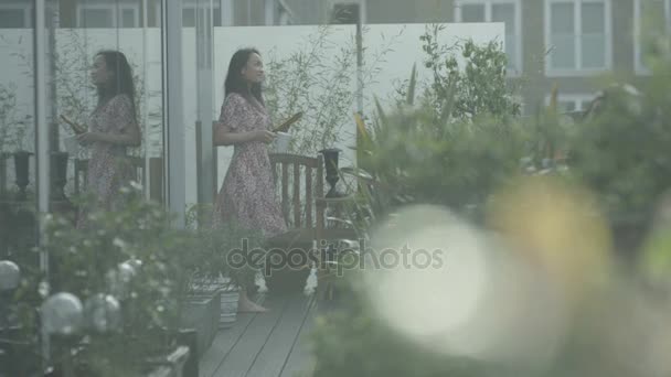 4K Young woman relaxing with computer tablet in apartment roof garden in the city
