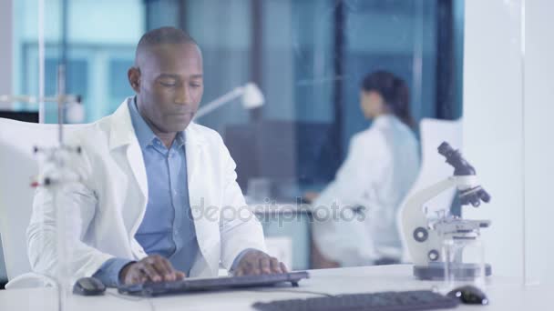 Scientifique masculin 4K en manteau blanc utilisant un écran tactile interactif dans un laboratoire moderne 