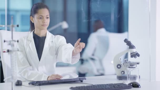 Femme scientifique 4K en manteau blanc en utilisant un écran tactile interactif dans un laboratoire moderne 