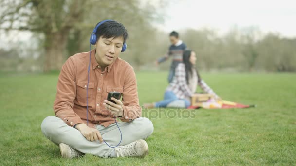 Hombre Escuchando Música Parque Con Madre Hijo Fondo — Vídeos de Stock