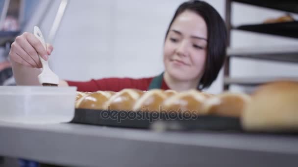 快乐的年轻工人在面包店厨房刷釉面包 — 图库视频影像