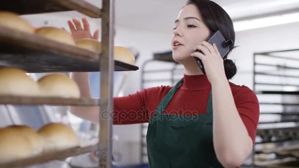 Εργαζόμενος Φούρνο Κουζίνας Μιλώντας Στο Τηλέφωνο Όπως Ελέγχει Δίσκοι Ψωμιού — Αρχείο Βίντεο