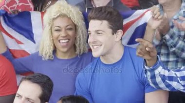 4k İngiliz bayrağı tutan genç kadın spor olay, kalabalığa oturan Çift
