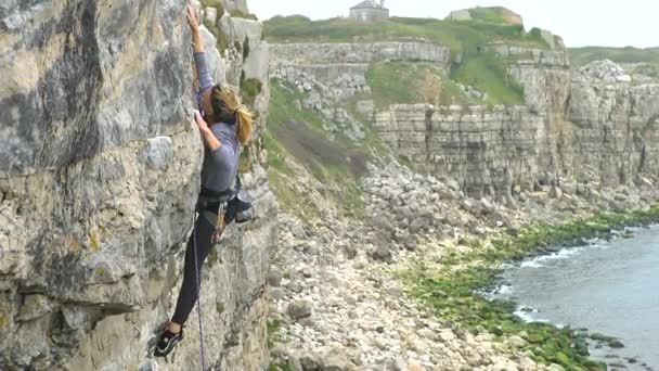 英語の海岸線に岩の崖を登って の若い女性 — ストック動画