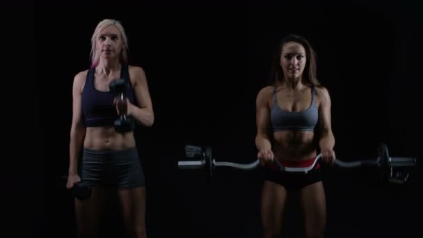 Zwei Fitte Junge Frauen Trainieren Mit Gewichten Vor Schwarzem Hintergrund — Stockvideo