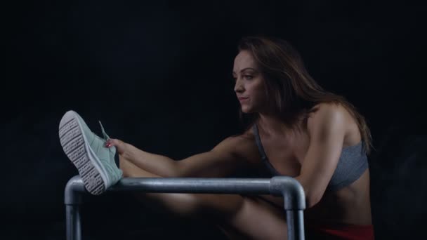 フィット若い女性黒の背景に足の筋肉を伸ばし — ストック動画