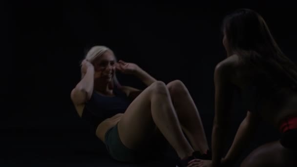 两个适合的女人在工作 一个女人做仰卧起坐 而另一个人抱着她的脚 — 图库视频影像
