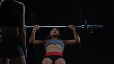 4k uygun genç kadının kişisel antrenör izlerken barbell bench press yapması