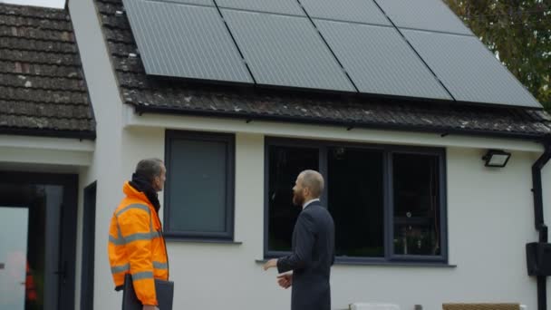 のビジネスマンとエンジニア住宅で屋根の上の太陽電池パネルを議論します — ストック動画