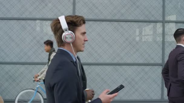 リラックスとして動作するように歩いて彼の実業家身に着けているヘッドフォン — ストック動画