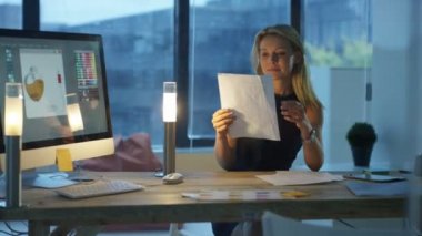 Tasarımcı geç saatlere kadar ofiste, bilgisayarda çalışarak ve telefon görüşmesi.