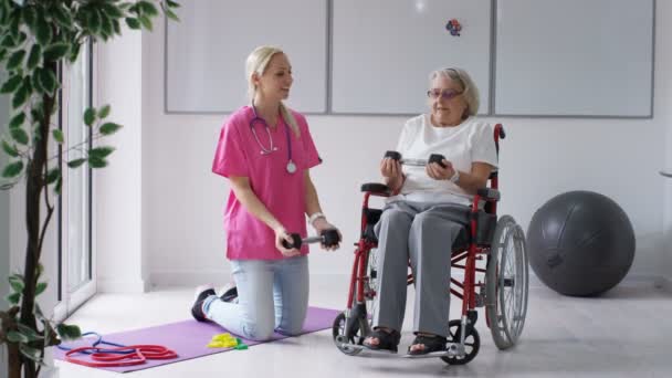 有料老人ホームで看護師は車椅子で年配の女性を示す重みを持ついくつかの演習 — ストック動画