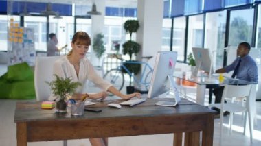 Beyaz işkadını arka plan üzerinde çalışma arkadaşları ile modern ofis masasında, cep telefonuyla konuşurken.