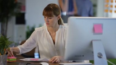 Beyaz işkadını modern ofisindeki bilgisayarda çalışma geçmiş meslektaşları ile çalışma.