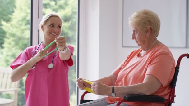 在寄宿护理院的护士向坐在轮椅上的老太太展示一些带有抵抗力的练习 — 图库视频影像