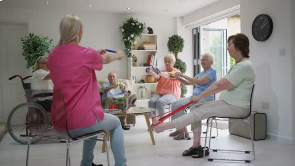 特別養護老人ホームで高齢者群の抵抗バンドをもついくつかの演習を示す若い看護師 — ストック動画