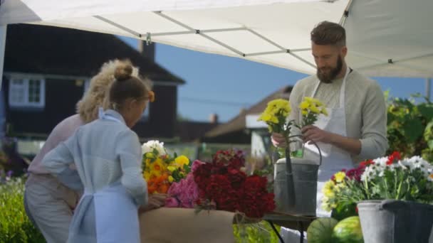 小女孩与二个成人在农夫市场上花摊位工作 — 图库视频影像