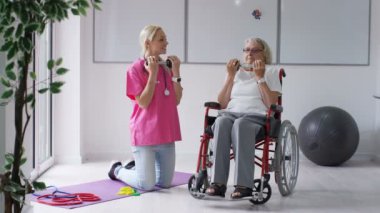 Yatılı bakım ev hemşire yaşlı Bayan tekerlekli sandalyede ağırlıklar ile bazı egzersizleri gösterilen.